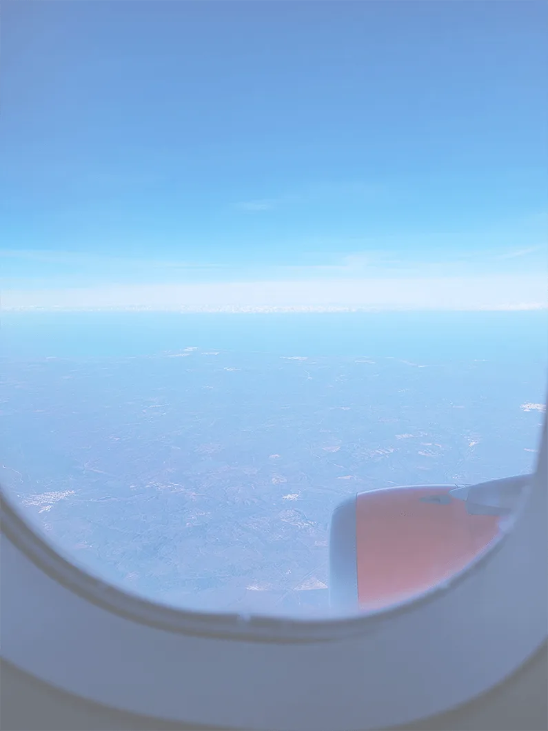 View from an airplane window: blue sky, horizon and part of an orange engine nacelle.