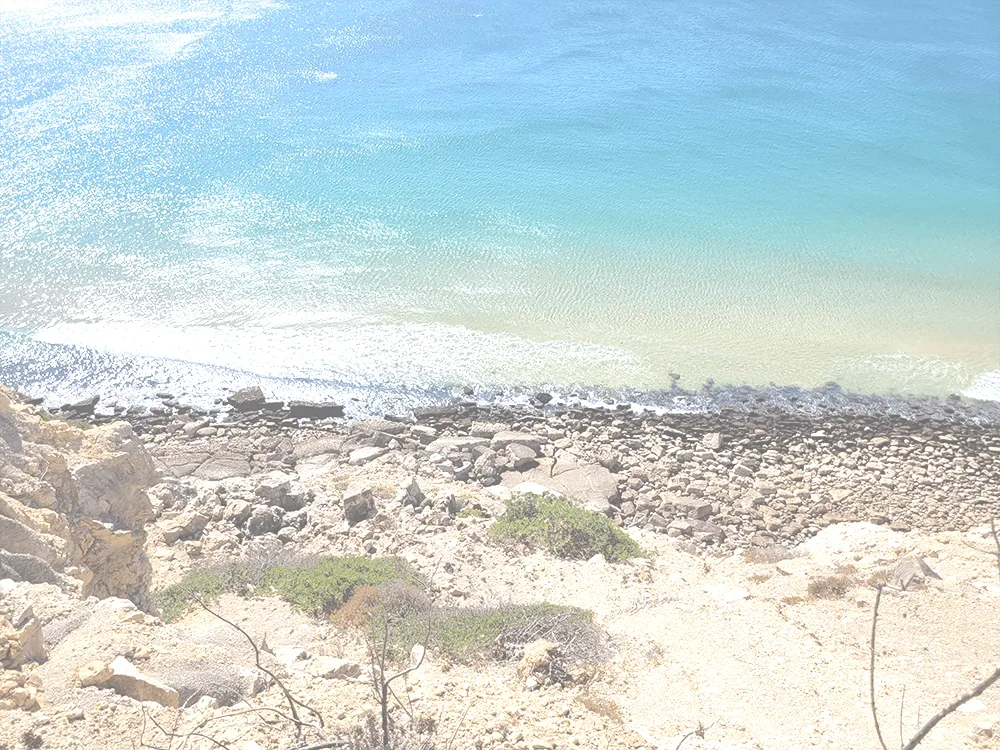 Rocky shoreline along a calm, turquoise-blue sea with gentle waves washing onto pale stones.